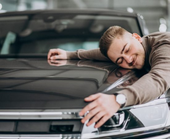 luxe car rental Young handsome man hugging a car in a car showroom